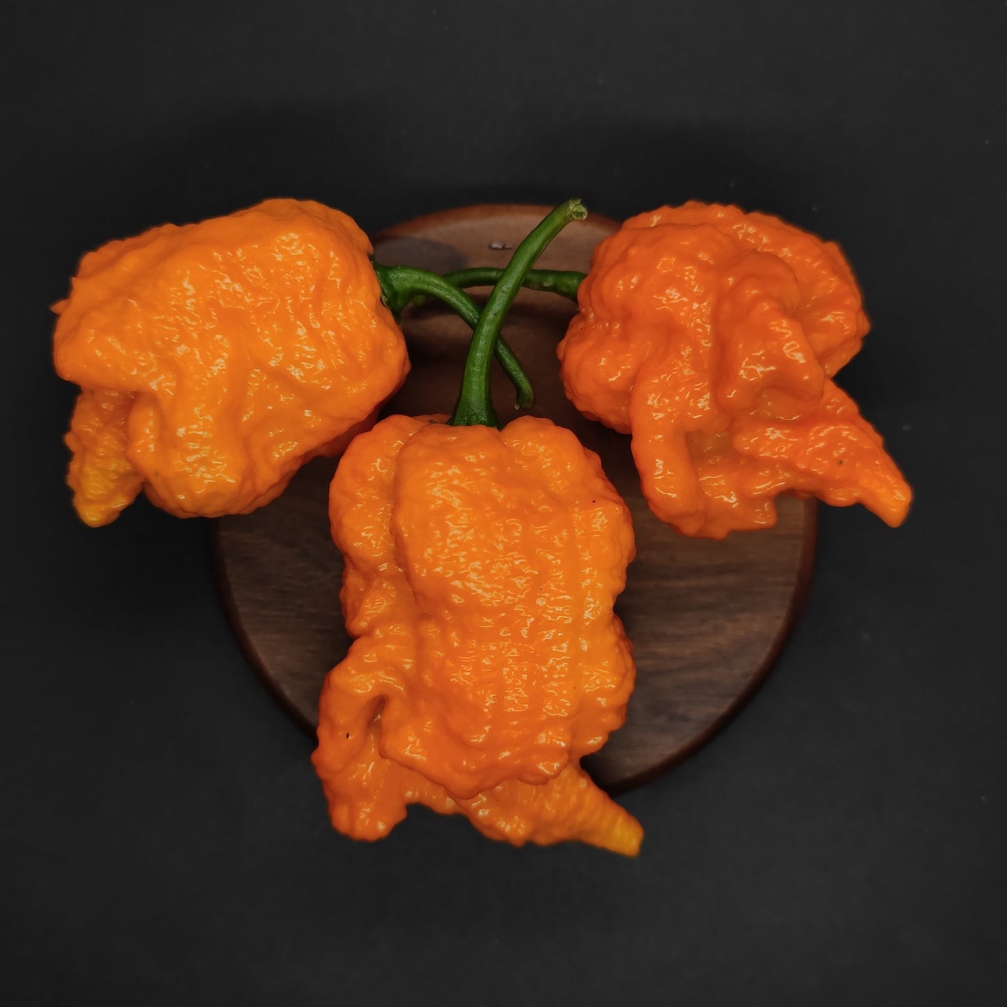 Three crispy pieces of Fried Chicken from PepperMerchant.net are arranged on a dark round wooden surface, set against a black background.