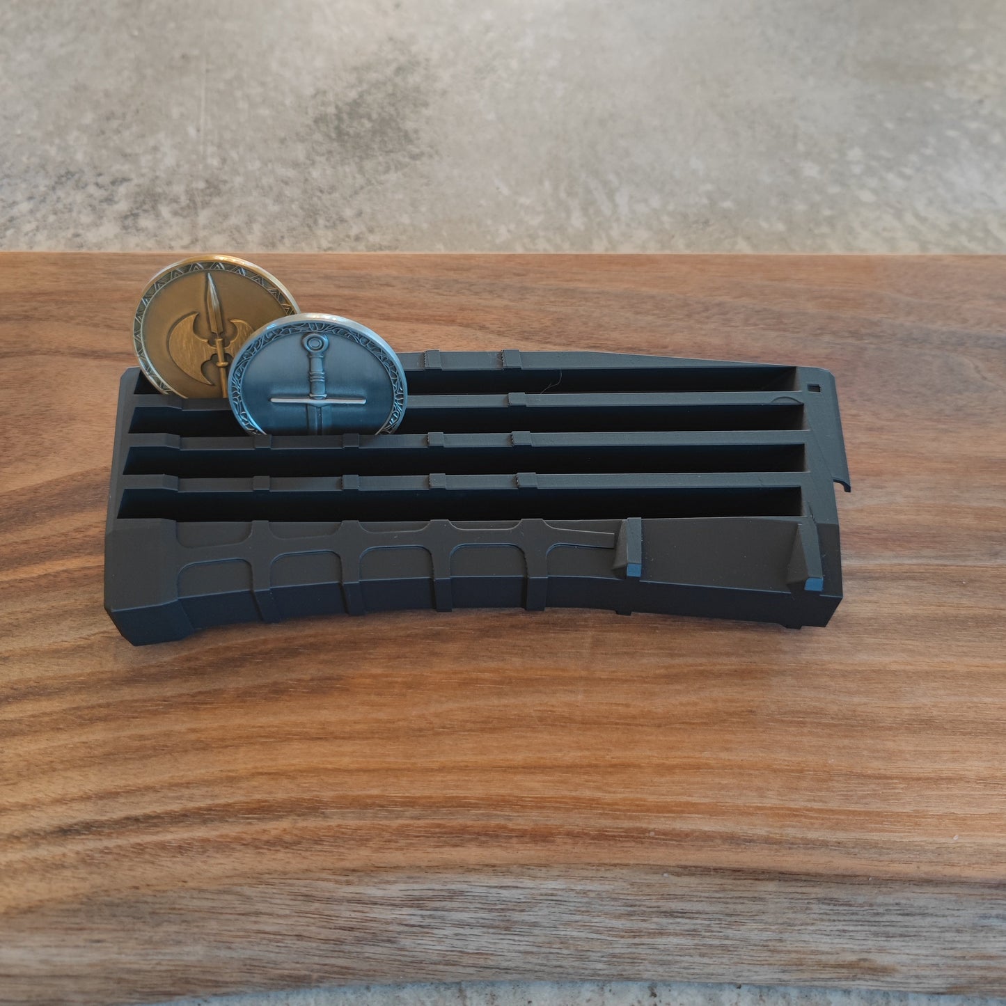 The GEN4 CoinMag - Black by coin-mag.net displays two collectible coins—one gold, one silver—in an upright position on a wooden surface, featuring a geometric design against a neutral textured background.