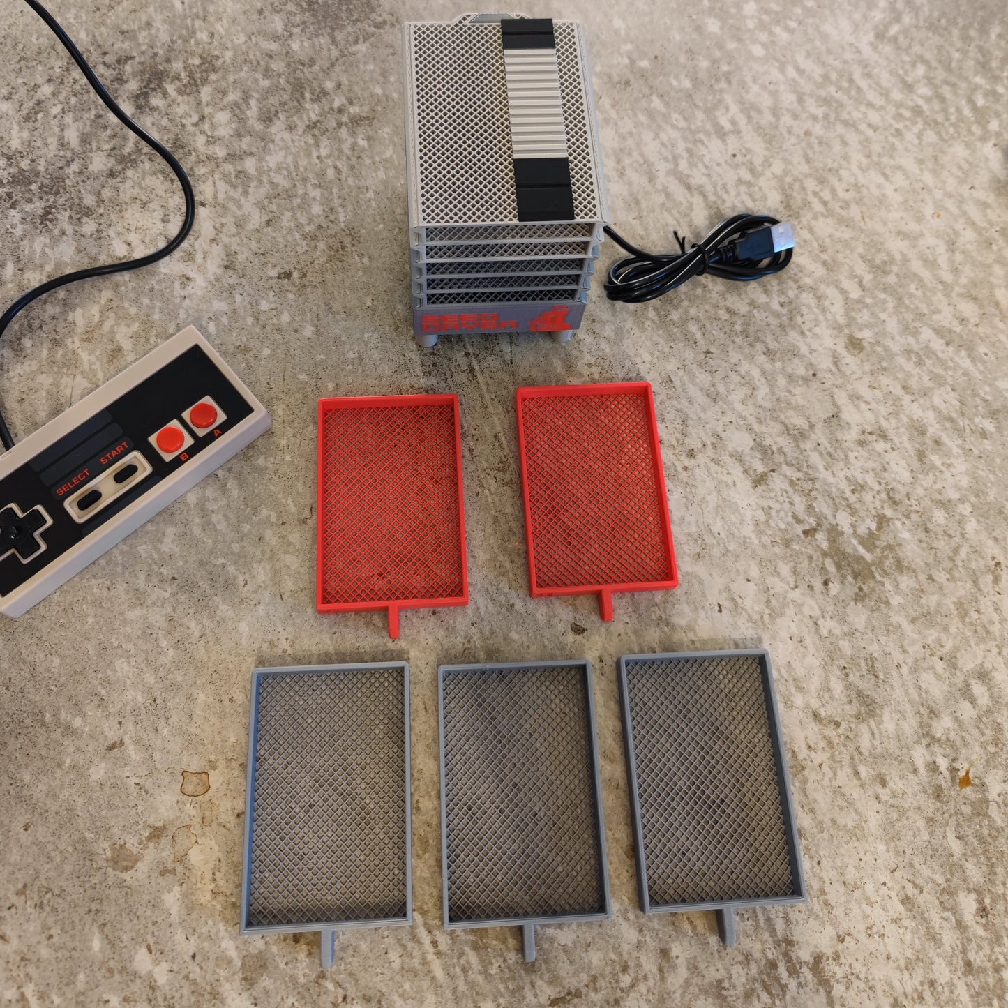 The Seed Dryer - Classic Console by PepperMerchant.net resembles a mini NES with mesh trays, controller, power cord, two red and three gray trays—combining innovative seed-saving technology with fun retro style.