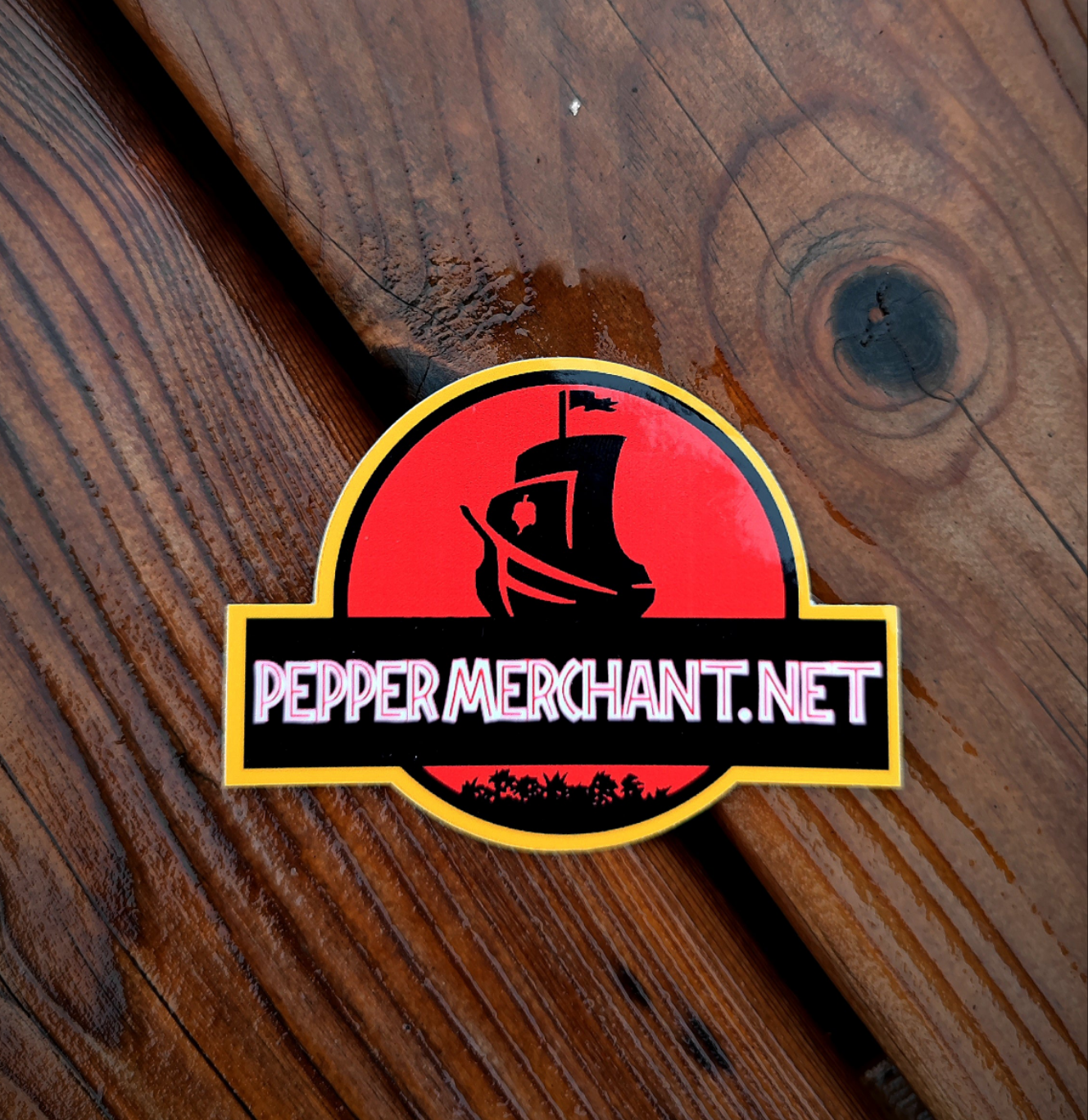 The Parklands Sticker by PepperMerchant.net shows a black ship silhouette on a red background with "PEPPER MERCHANT.NET" in bold white letters, displayed on a wooden surface.