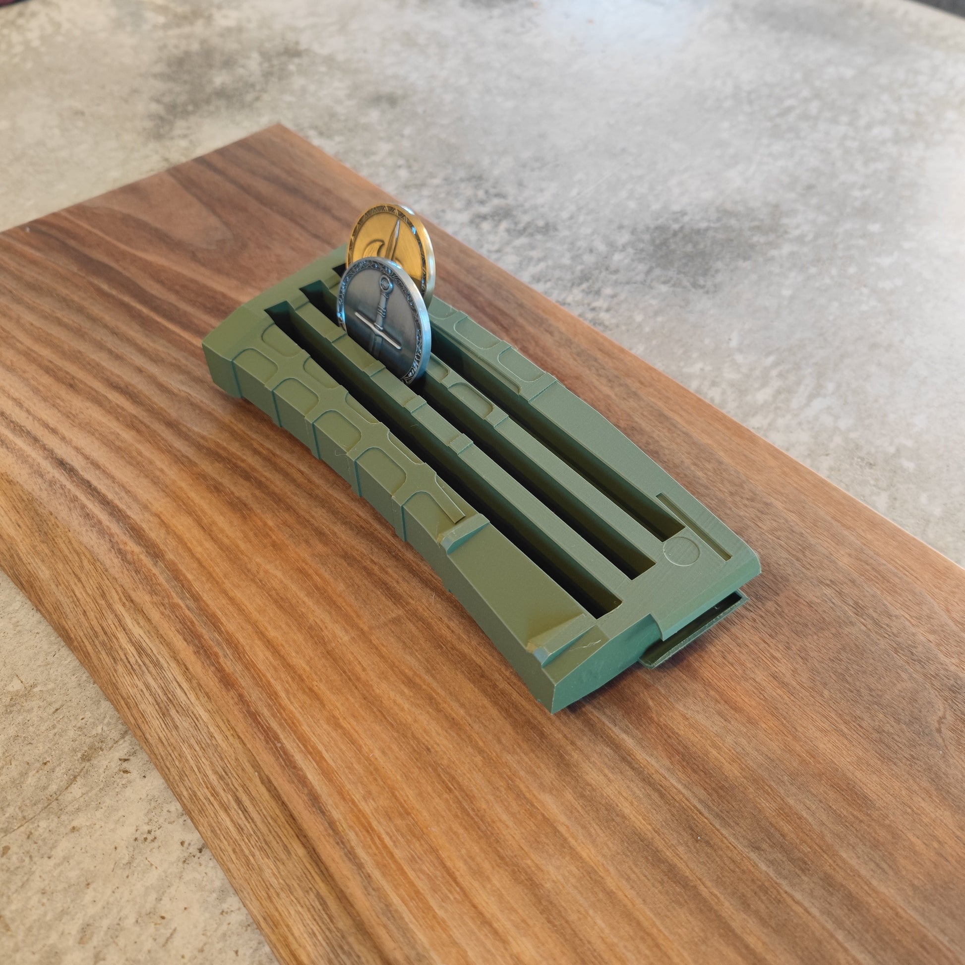 The GEN3 CoinMag - Olive by coin-mag.net is a green, rectangular coin holder that elegantly displays two coins on a polished wooden board, perfect for collectors seeking a sleek challenge coin display.