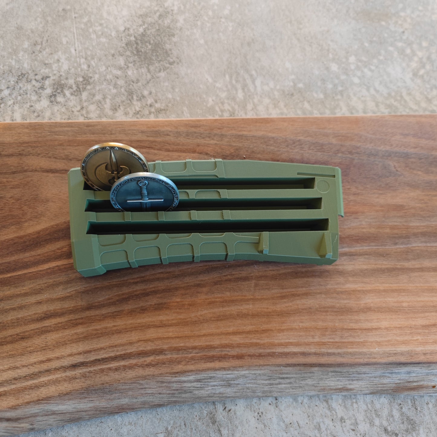 The GEN3 CoinMag - Olive by coin-mag.net showcases two round, military-style coins in a green, magazine-style display on a wooden surface against a gray background.