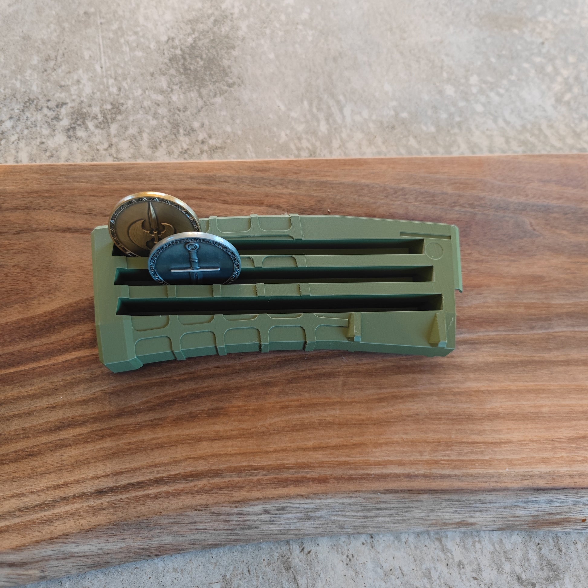 The GEN3 CoinMag - Olive by coin-mag.net showcases two round, military-style coins in a green, magazine-style display on a wooden surface against a gray background.