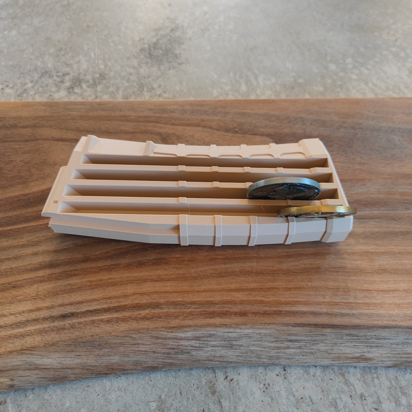 The GEN4 CoinMag - Sand by coin-mag.net, a beige 3D-printed challenge coin holder with grooves, displays two coins on a wooden surface against a gray, textured background.