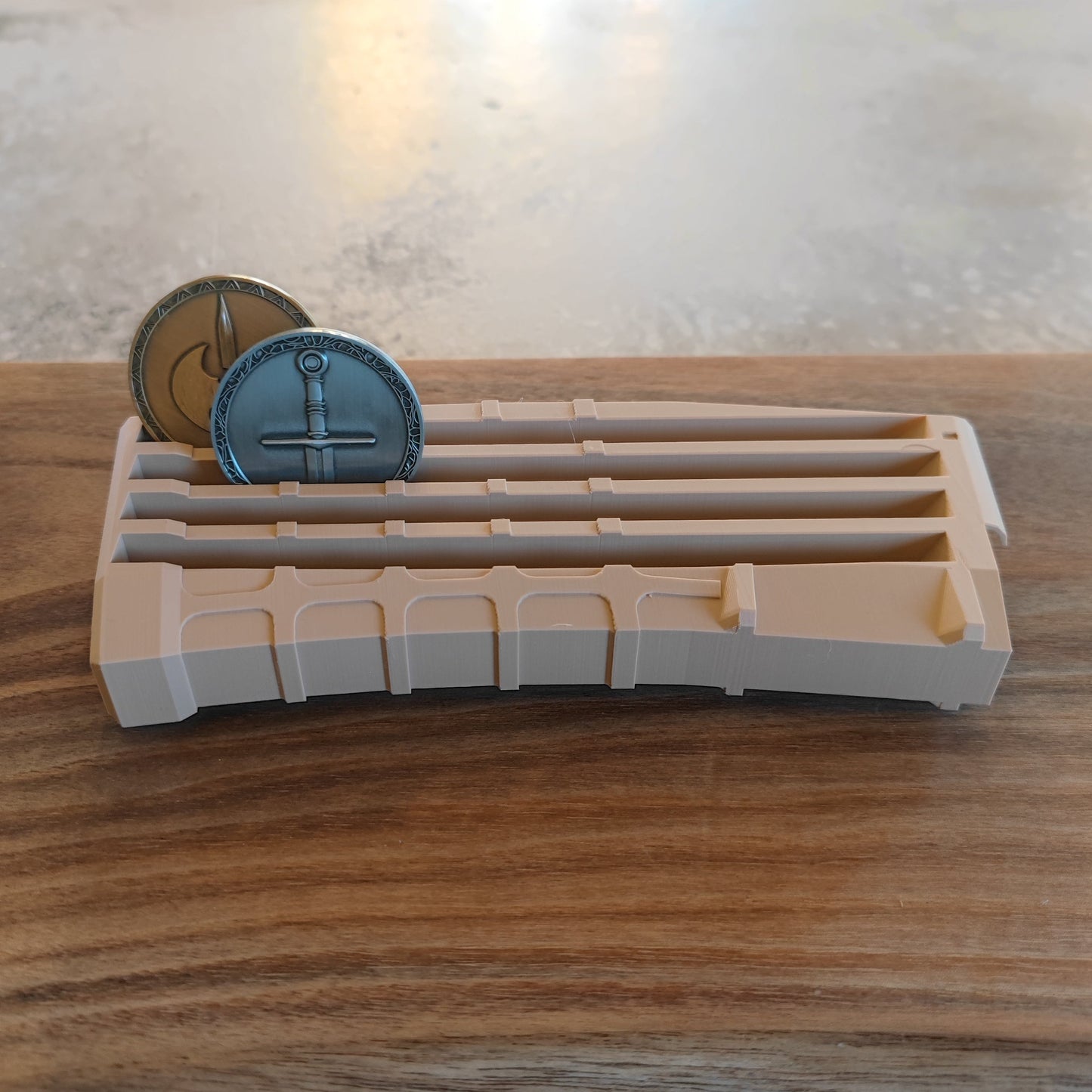 The GEN4 CoinMag - Sand by coin-mag.net sits on a wooden surface, elegantly displaying two upright fantasy coins—one gold and one silver—in separate slots.