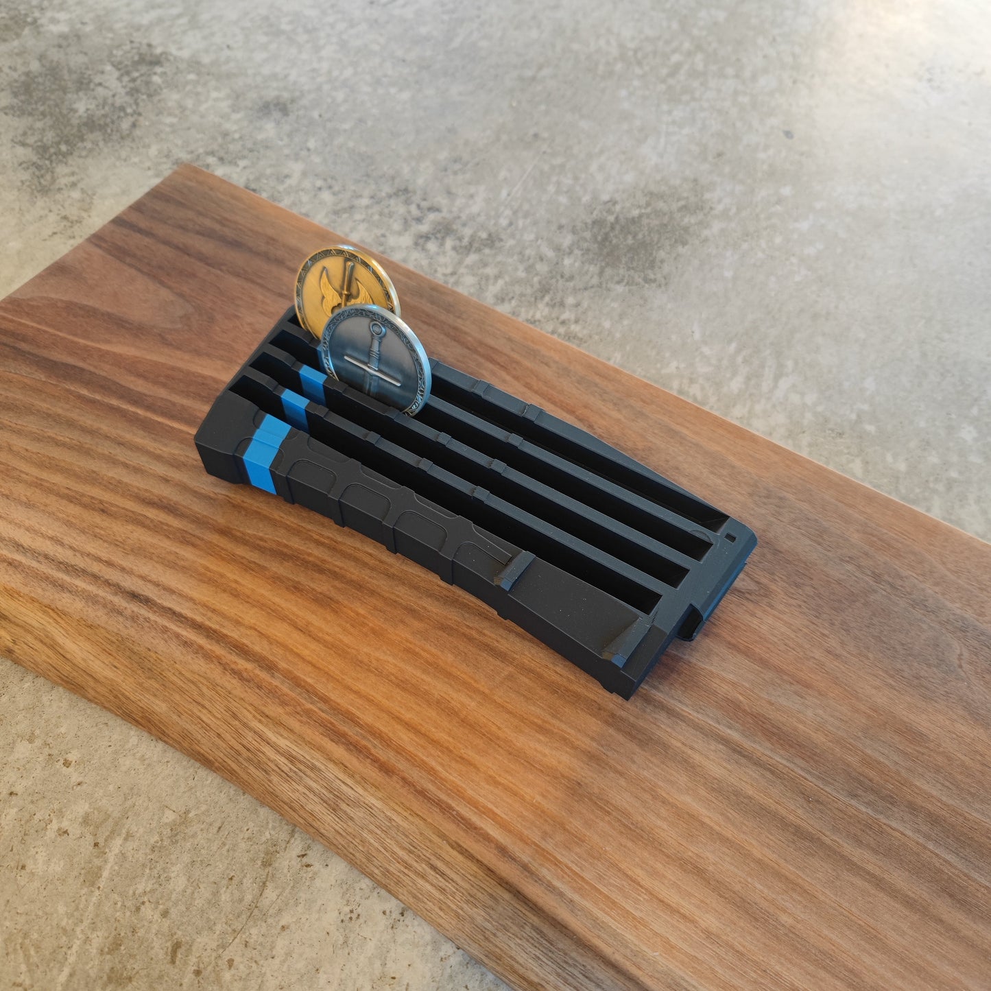 The GEN4 CoinMag - Blue Line by coin-mag.net, a black and blue challenge coin holder with two coins inserted, rests on a rectangular wooden board placed on concrete.