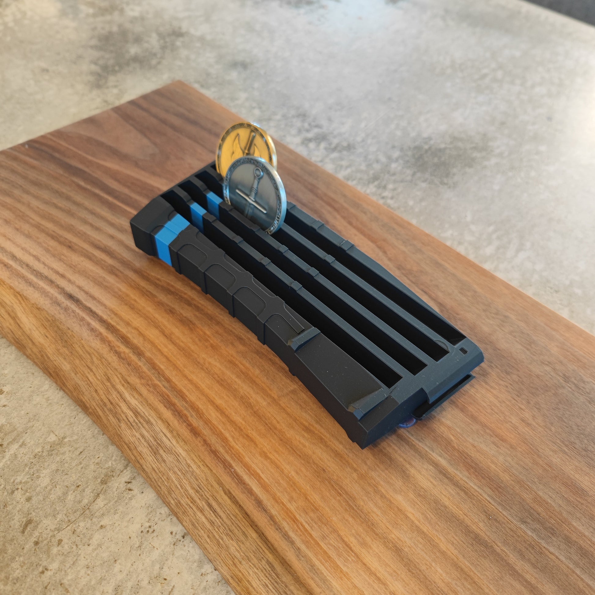 The GEN4 CoinMag - Blue Line from coin-mag.net is a black and blue plastic holder that displays two coins upright on a rectangular wooden base, shown here resting on a stone surface.