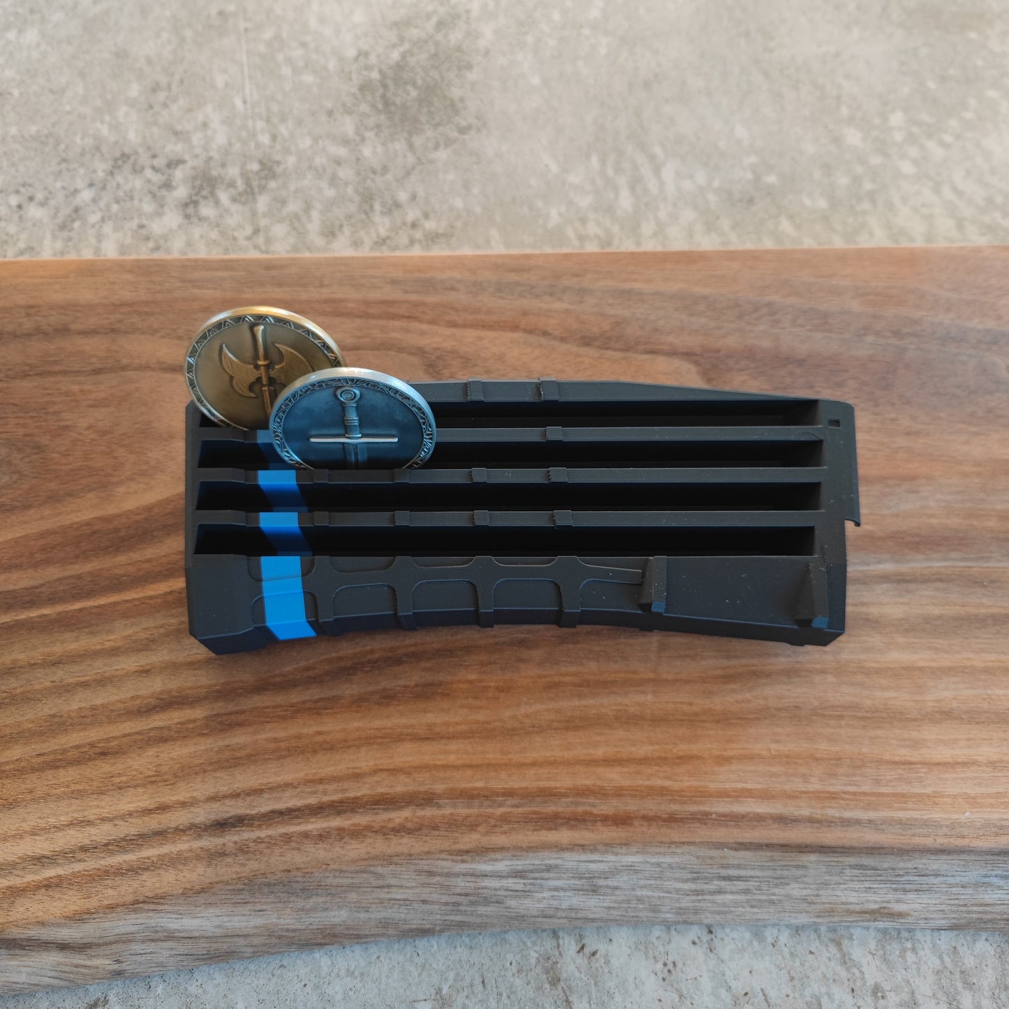The GEN4 CoinMag - Blue Line by coin-mag.net, a black plastic display with a blue stripe, holds two commemorative coins on a wooden surface with a concrete background.