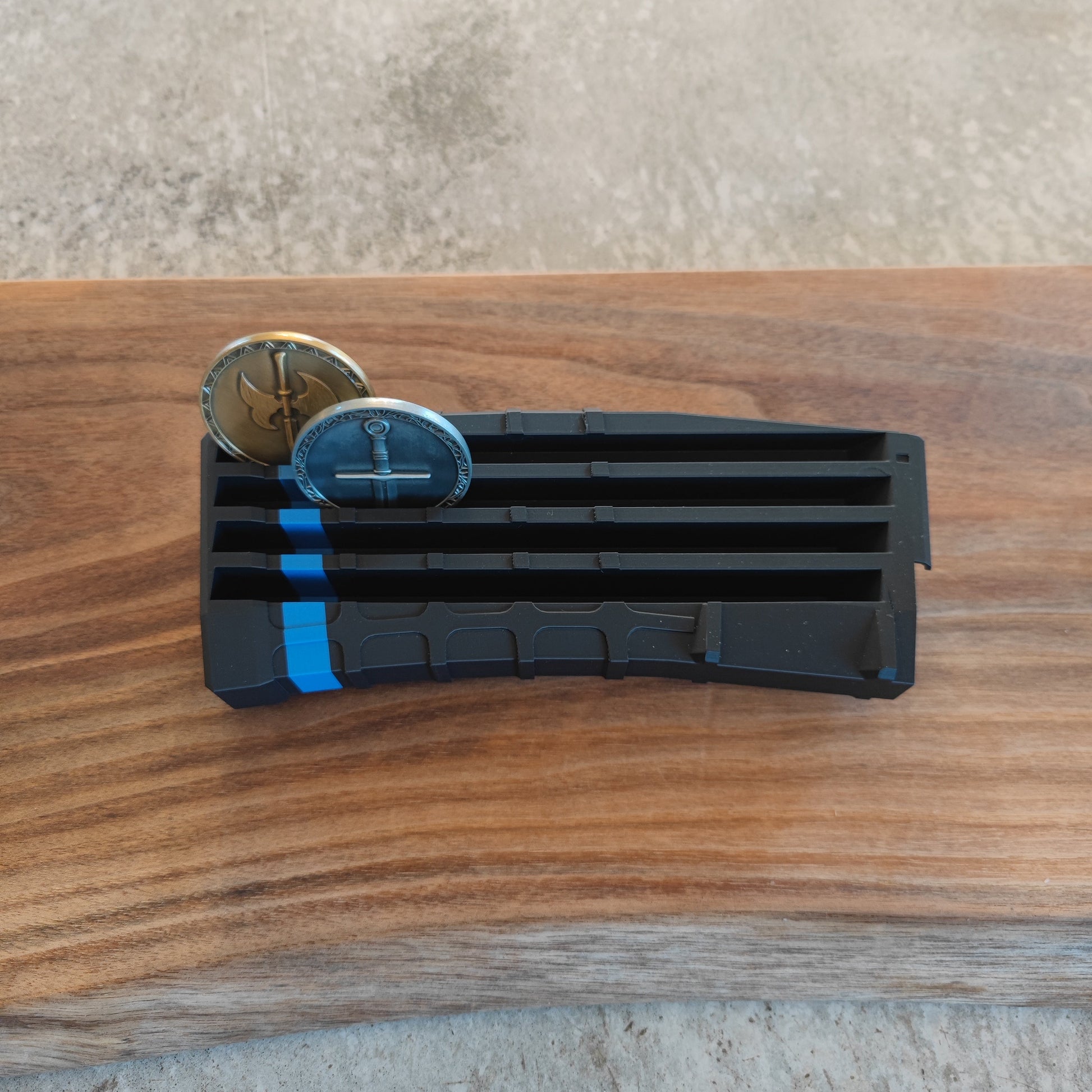 The GEN4 CoinMag - Blue Line by coin-mag.net, a black plastic display with a blue stripe, holds two commemorative coins on a wooden surface with a concrete background.
