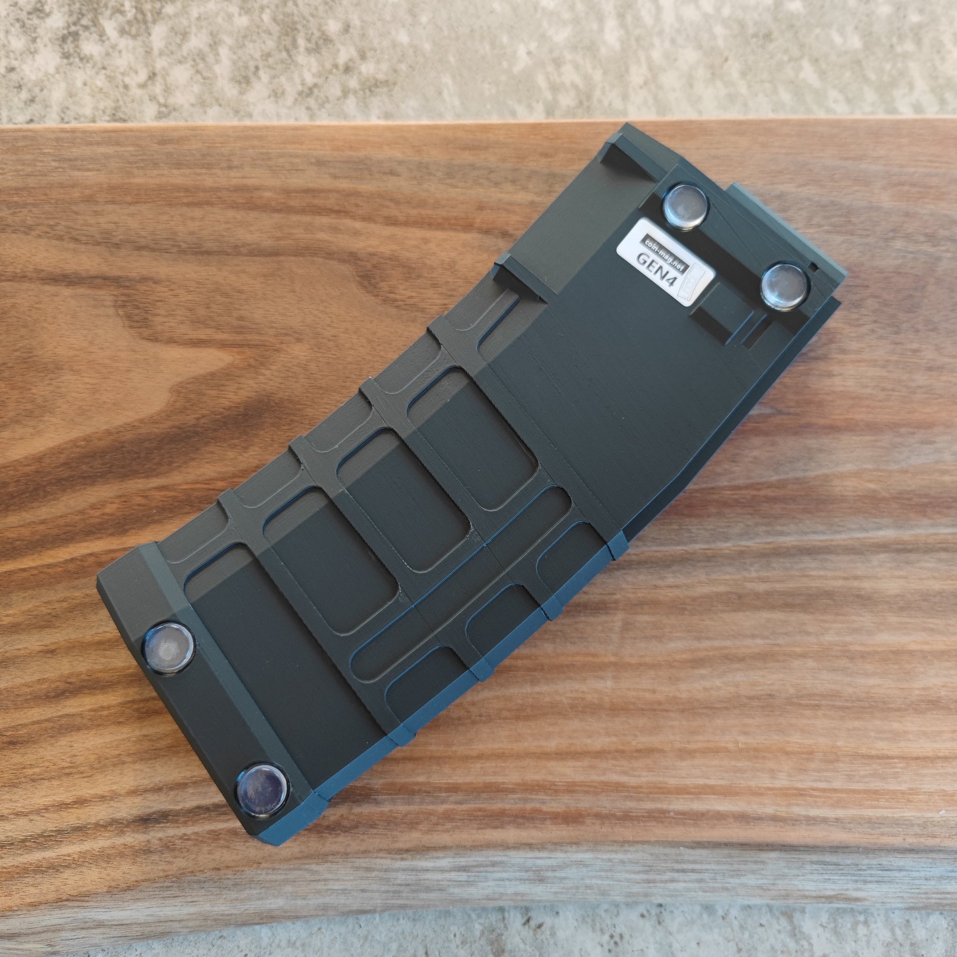 The GEN4 CoinMag - Black from coin-mag.net is a black, rectangular coin holder with ridges, rounded corners, four visible screws, and a small "GEN 4" label—ideal for challenge coin collectors.