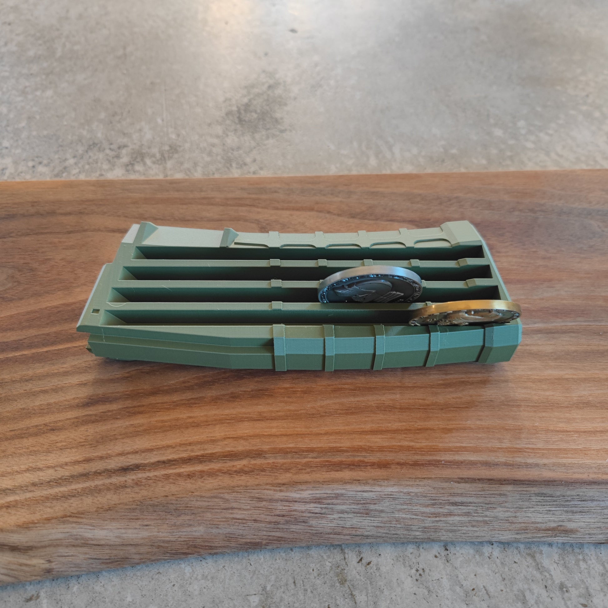 The GEN4 CoinMag - Olive by coin-mag.net is a green plastic organizer with multiple slots for coins, shown holding two watches on a wooden surface against a gray, textured background.