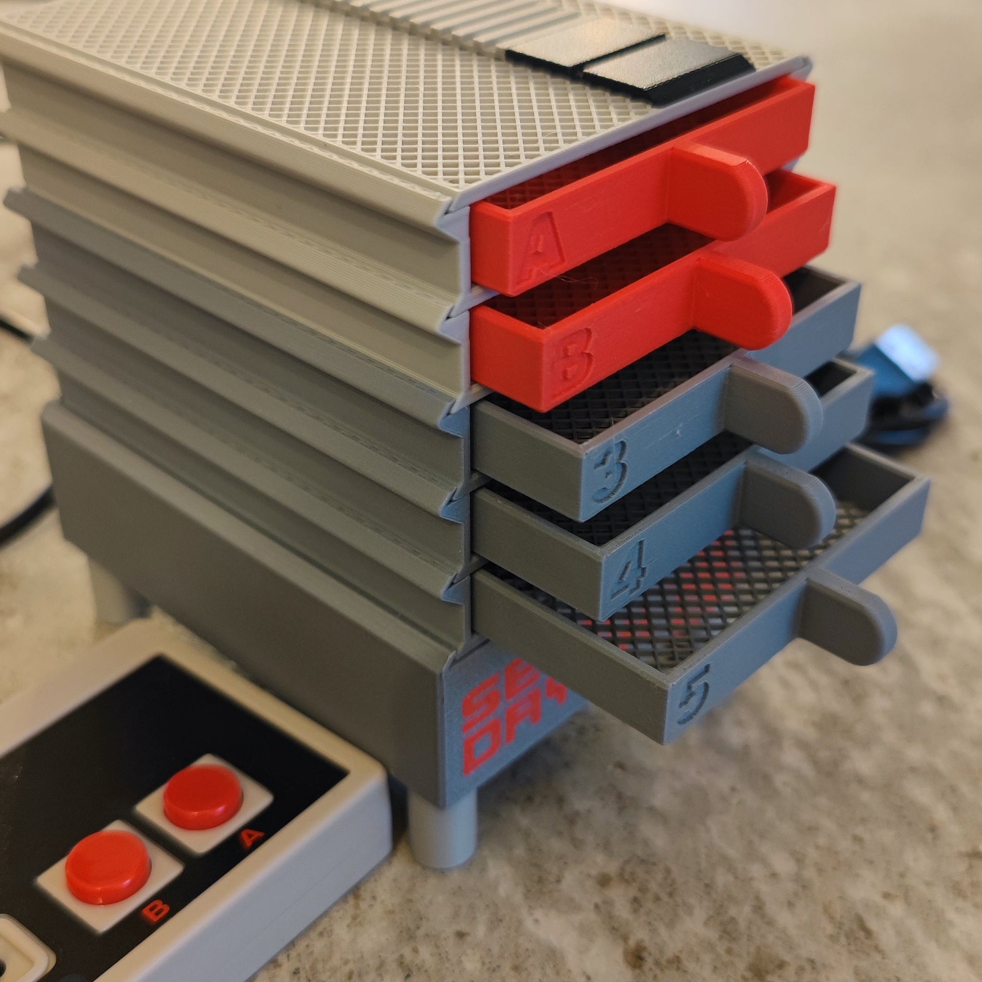 A stackable storage rack with red "A" and "B" tabs and gray trays numbered "3," "4," and "5" is shown. Nearby is the Seed Dryer - Classic Console by PepperMerchant.net, next to a retro-style game controller, highlighting modern seed saving.