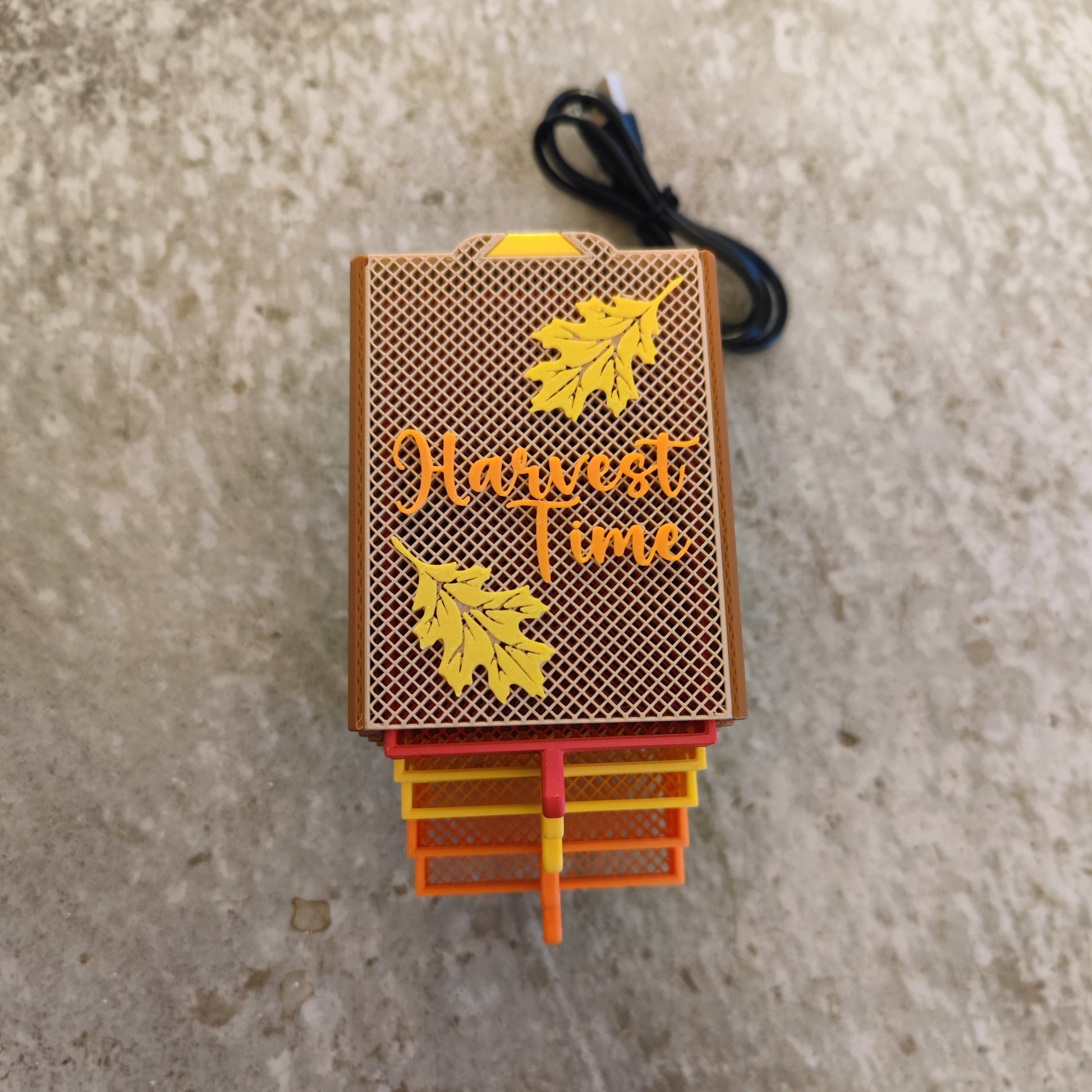 The PepperMerchant.net Seed Dryer - Harvest Time features a decorative fall-themed box with yellow leaves and "Harvest Time" on top, perfect for storing seed saving supplies. It rests on a textured surface with a black cord behind it.
