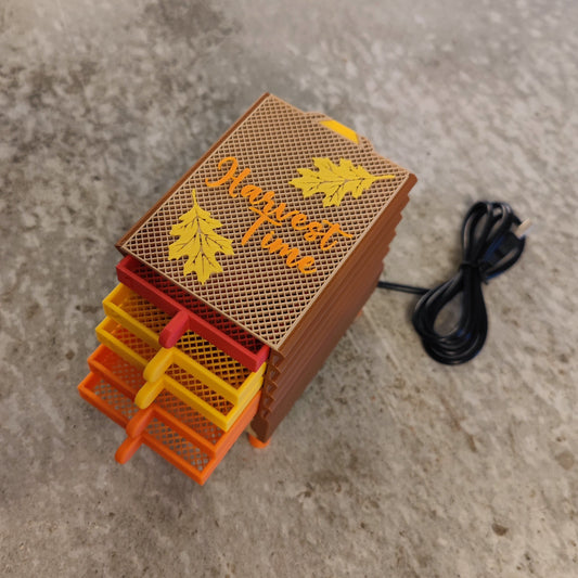 The Seed Dryer - Harvest Time by PepperMerchant.net is a small, brown heatless seed dryer with four orange and yellow sliding trays, two yellow leaves and text on the lid, plus a black power cord—perfect for saving seeds on your countertop.
