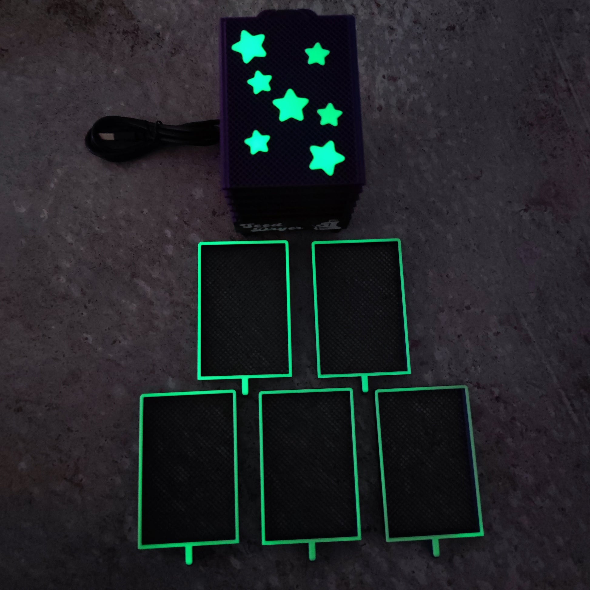 The PepperMerchant.net Seed Dryer - Nightshade (Glows) features a black box with glowing star shapes, a power cord, and five illuminated rectangular elements—showcasing advanced USB-powered seed drying technology.
