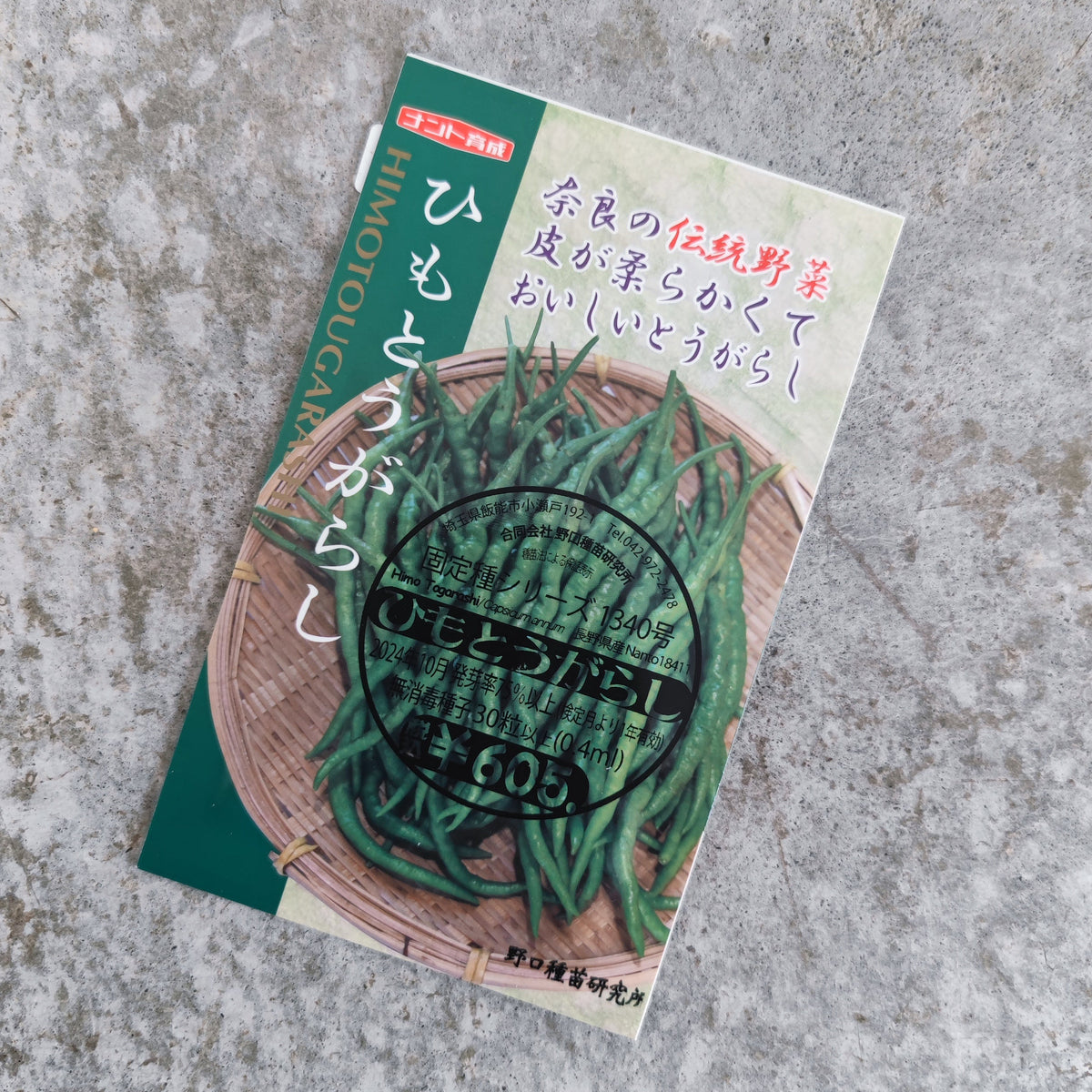 A packet of Himo Togarashi seeds from PepperMerchant.net featuring a circular stamp and an image of green Japanese pepper chilies in a woven basket.