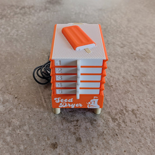 A PepperMerchant.net Seed Dryer - Creamsicle in small orange and white, featuring five numbered drawers, a white knob, and a black power cord, sits on a beige surface.