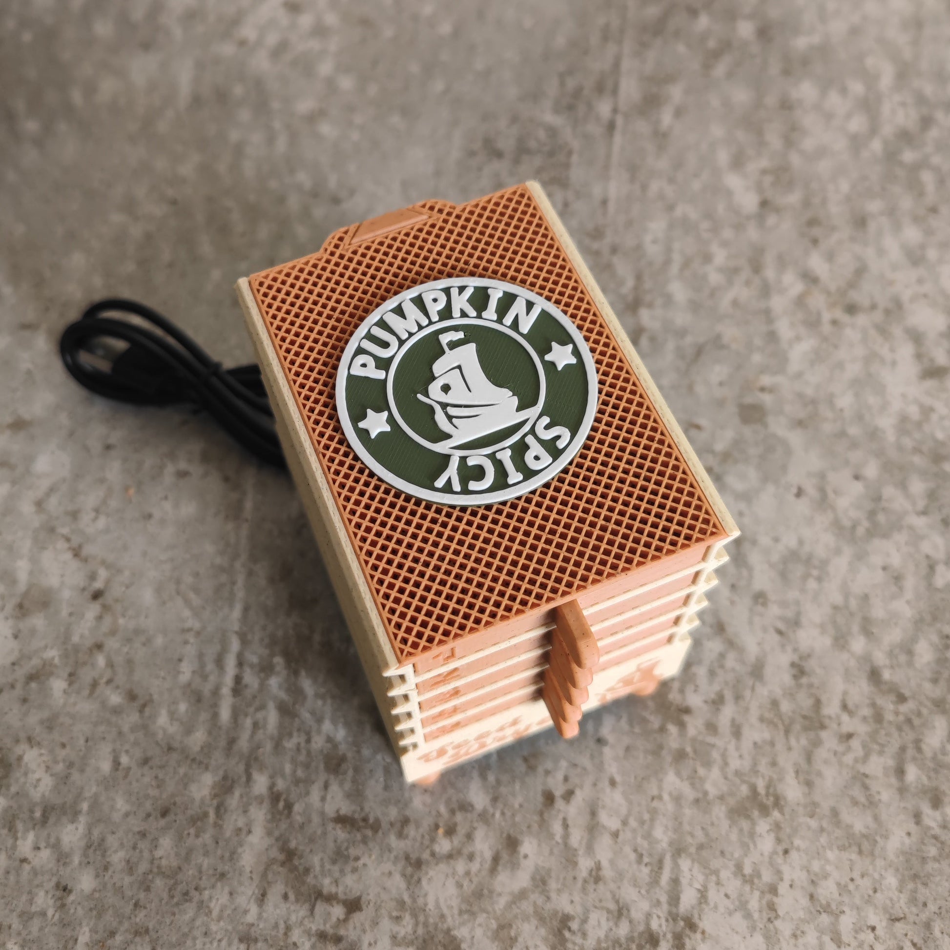 A compact, rectangular orange device labeled “Seed Dryer - Pumpkin Spicy *Limited Edition*” by PepperMerchant.net rests on a gray surface, with a black cord extending from one side—resembling a pumpkin spice–themed seed dryer perfect for seed savers.