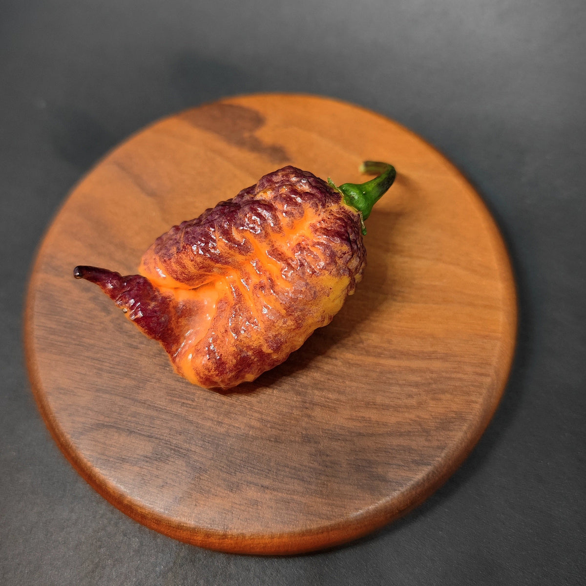 A bumpy, yellow and purple Reaper Sbagliato Carolina Reaper resting on a circular wooden board.