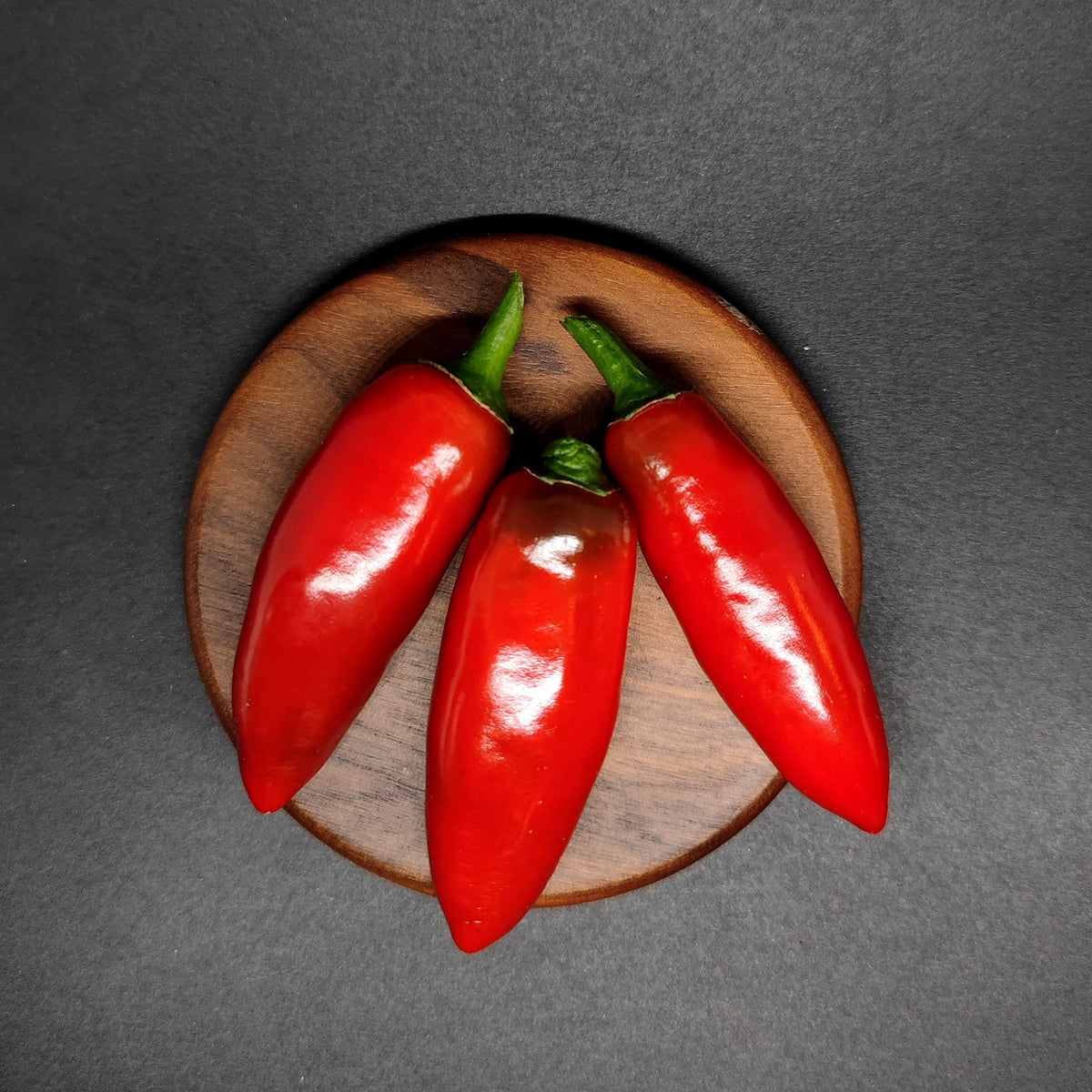 Three red Calabrian peppers on a small wooden plate.