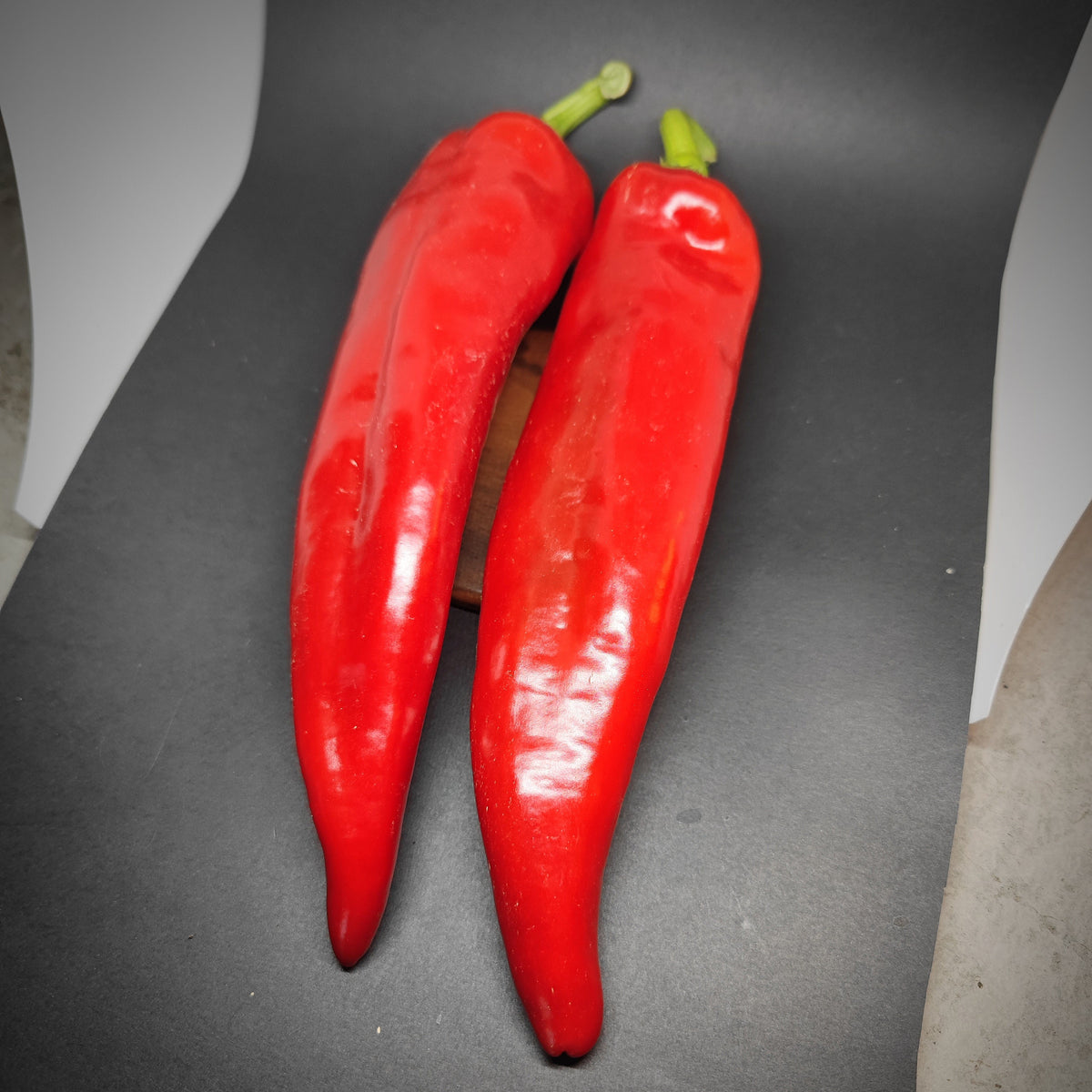 Two long, bright red Shepard Peppers with green stems.
