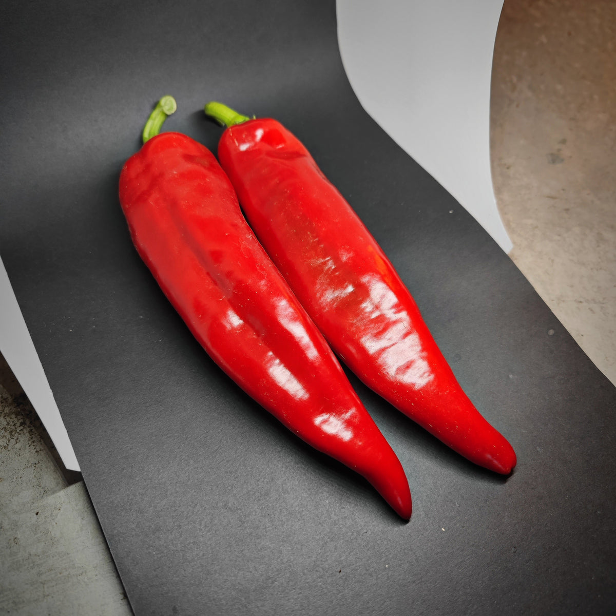 Two bright red Shepard peppers with green stems lying side by side.