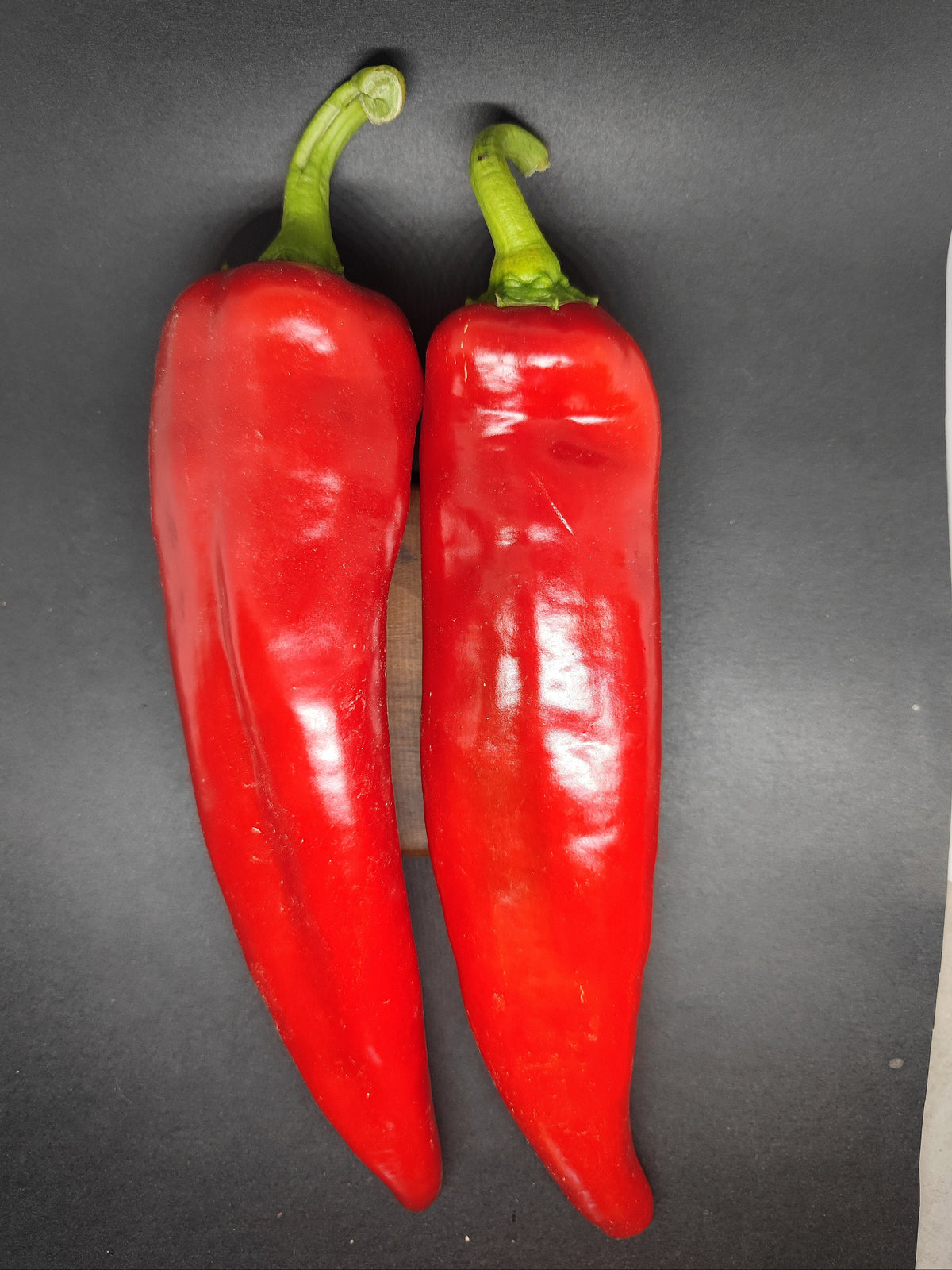 Two long, glossy red Shepard peppers with green stems placed side by side.