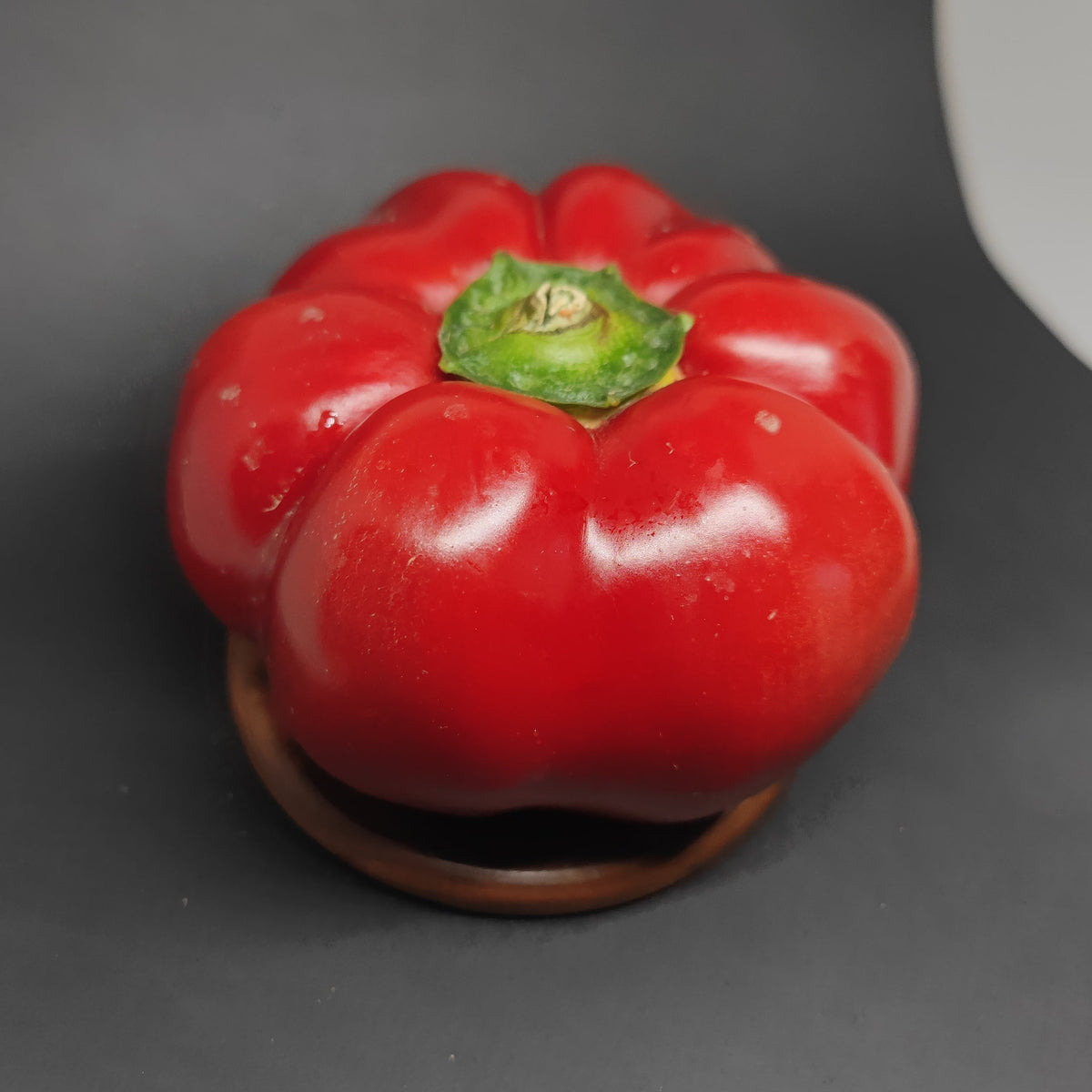 A round, shiny red Paprika with a green stem.