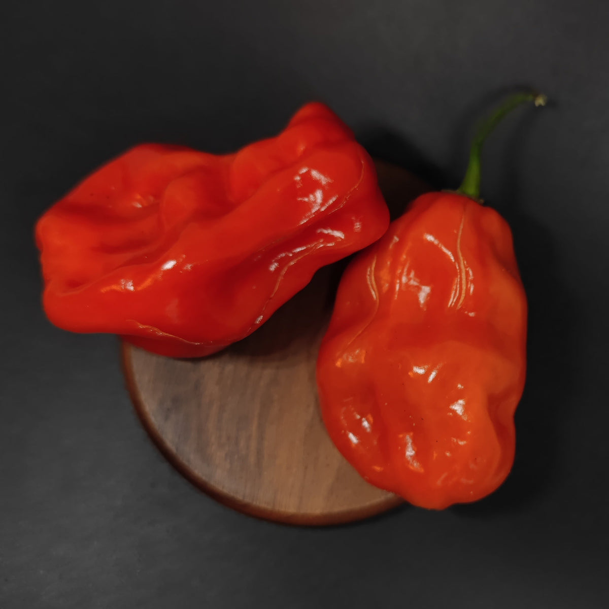 Two bright red, wrinkled Giant Habanero peppers resting on a small circular wooden board.