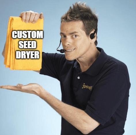A person with spiky hair and a headset is grinning ear to ear while holding up an orange cloth with the bold white text "CUSTOM SEED DRYER" emblazoned on it, possibly referring to the innovative Seed Dryer - Custom Design by PepperMerchant.net. The individual is dressed in a dark polo shirt.