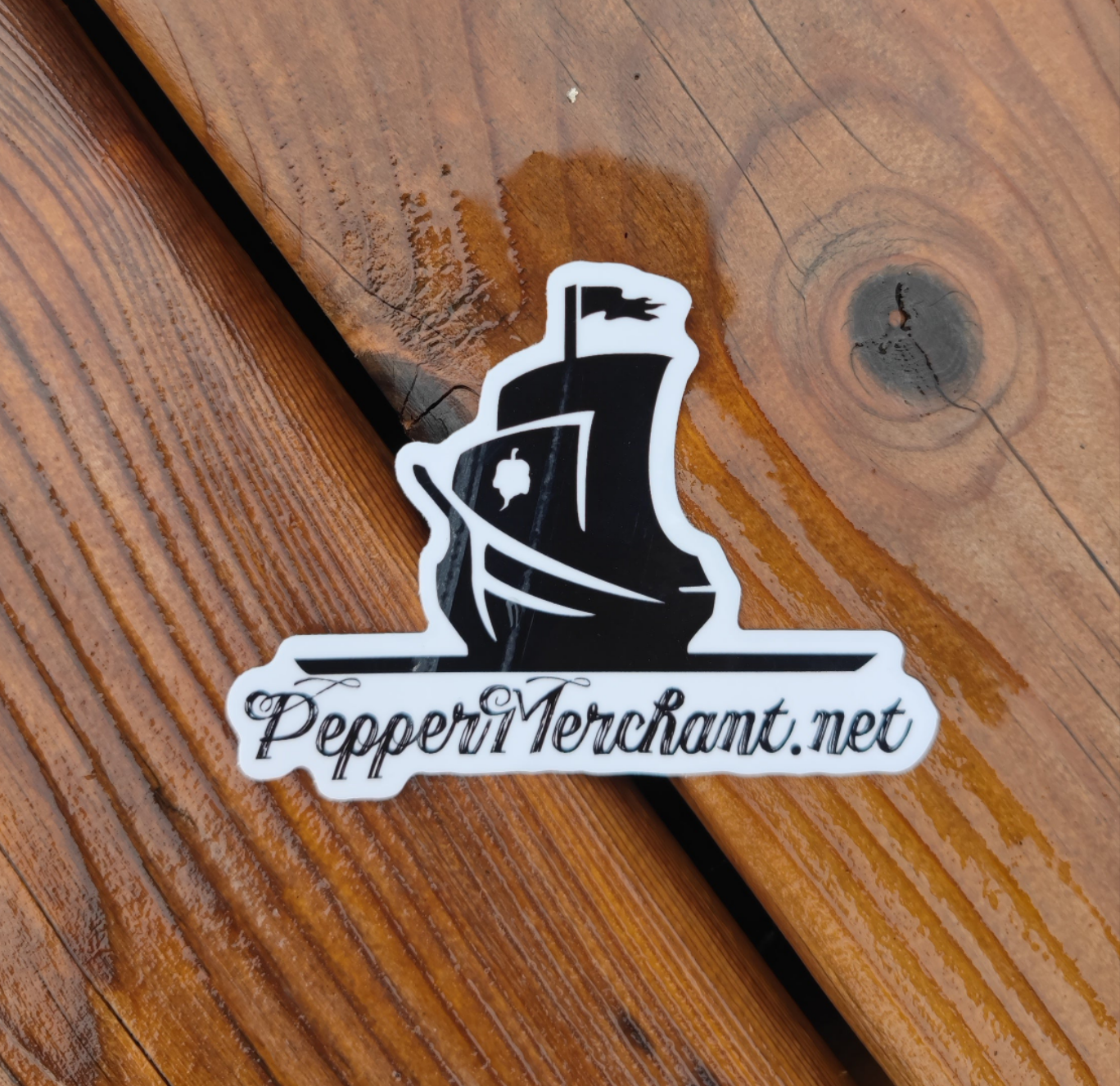 The PepperMerchant.net Sticker features a black pirate ship and "PepperMerchant.net" in decorative script on wood, reflecting the brand’s premium seeds and hydroponics focus.