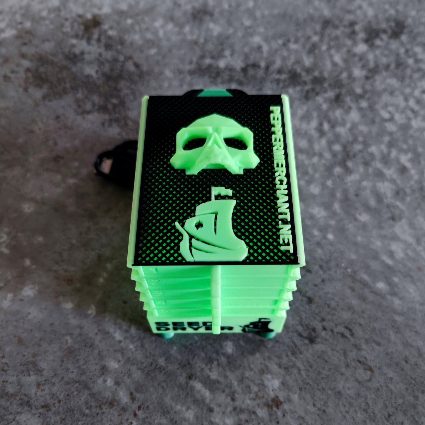 A glowing rectangular green Seed Dryer (Limited Edition) from PepperMerchant.net, featuring a skull and ship design with "PIRATESERVERCHAIN.NET" on the side—perfect for seed-saving tech enthusiasts.