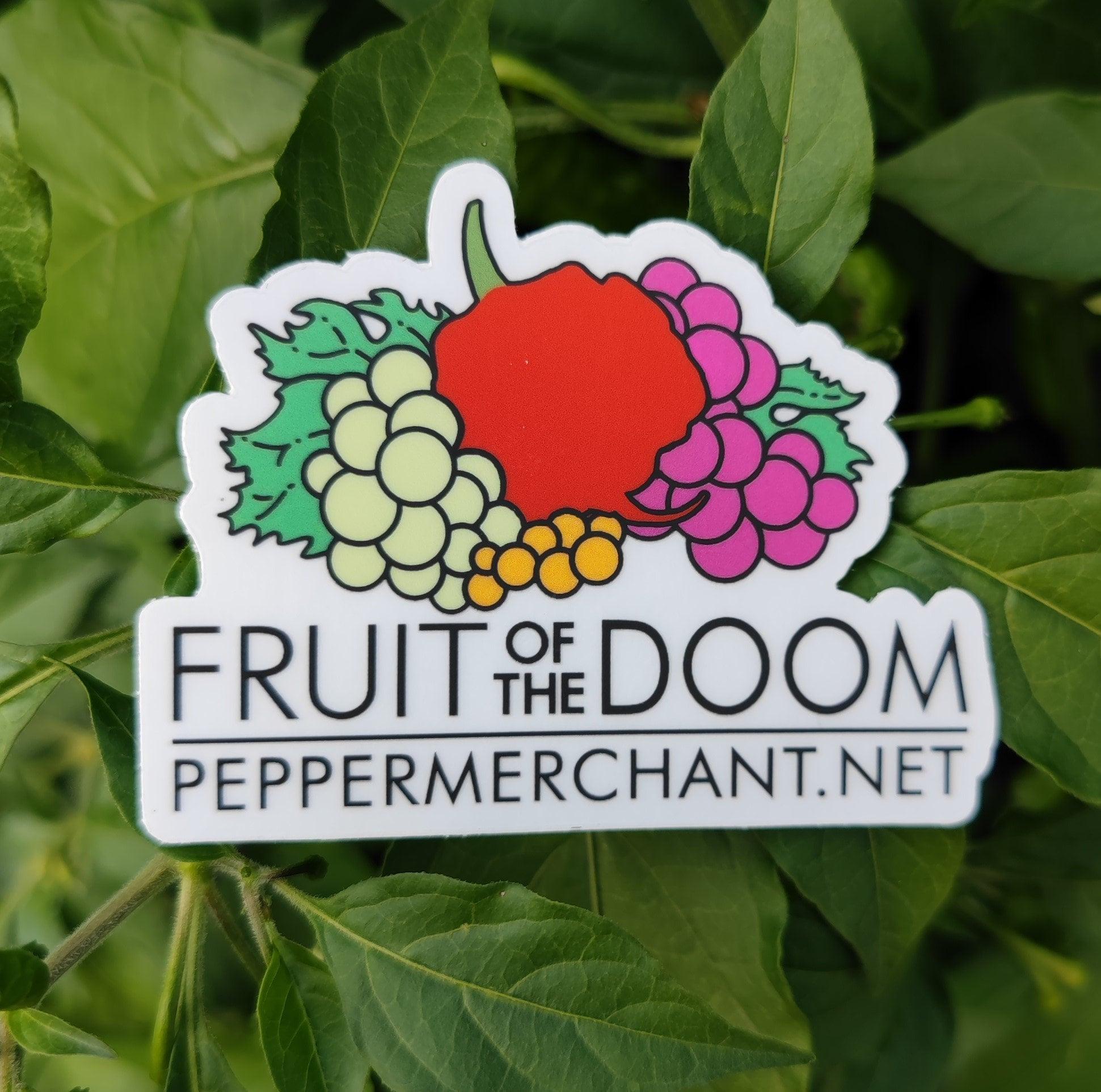 The Fruit of The Doom Sticker from PepperMerchant.net showcases a red pepper encircled by vibrant grapes and green leaves. The text "FRUIT OF THE DOOM" and "PEPPERMERCHANT.NET" is prominently displayed below the design, which is set against a close-up background of green leaves, making it pop on light-colored surfaces.