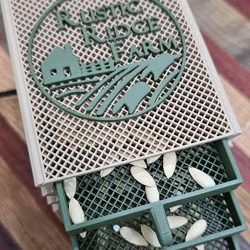 A compact green and beige Seed Dryer - Custom Design by PepperMerchant.net features divided compartments for drying pumpkin or squash seeds. It rests on a striped wooden surface, highlighting modern seed-saving solutions.