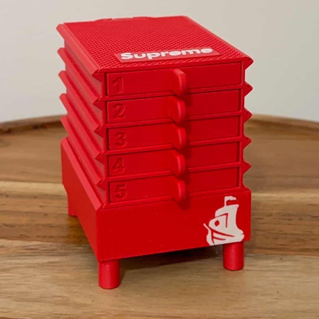 The Seed Dryer - Custom Design by PepperMerchant.net is a small red plastic cabinet with five numbered drawers, a white Supreme logo on top, and a graphic in the lower right—ideal for organizing seed drying tools—shown on a wooden surface.